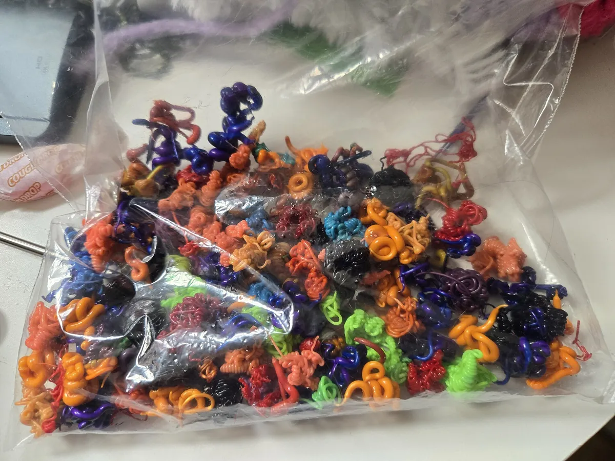A clear plastic bag full of small curled blobs of purged filament in orange, purple, black, green and red